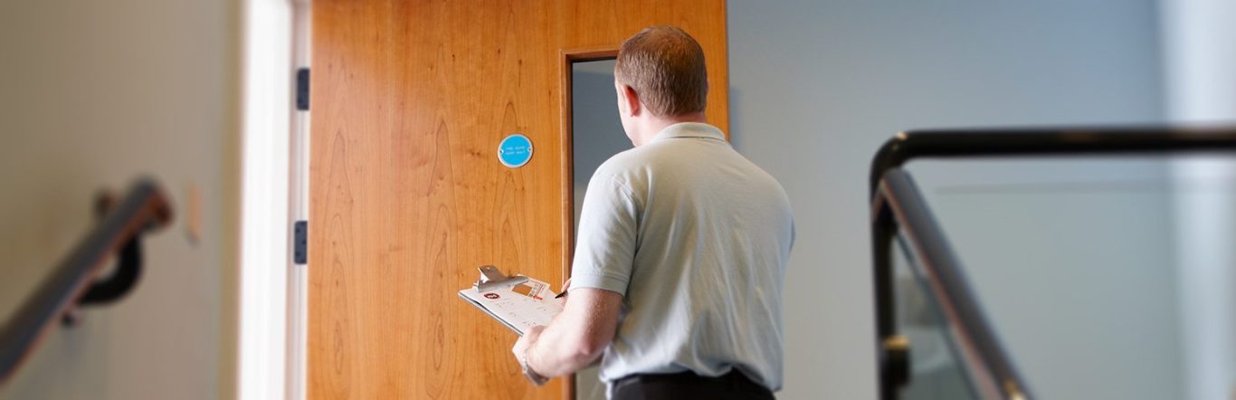 Un homme tenant une planche à clip se dirige vers une porte en bois.