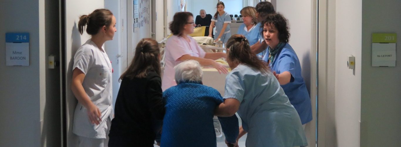 Un groupe de professionnels de santé aide une patiente dans un couloir d'hôpital.