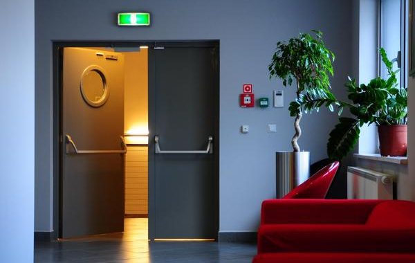 Porte ouverte vers une lumière chaleureuse, canapé rouge et plante en pot à côté.