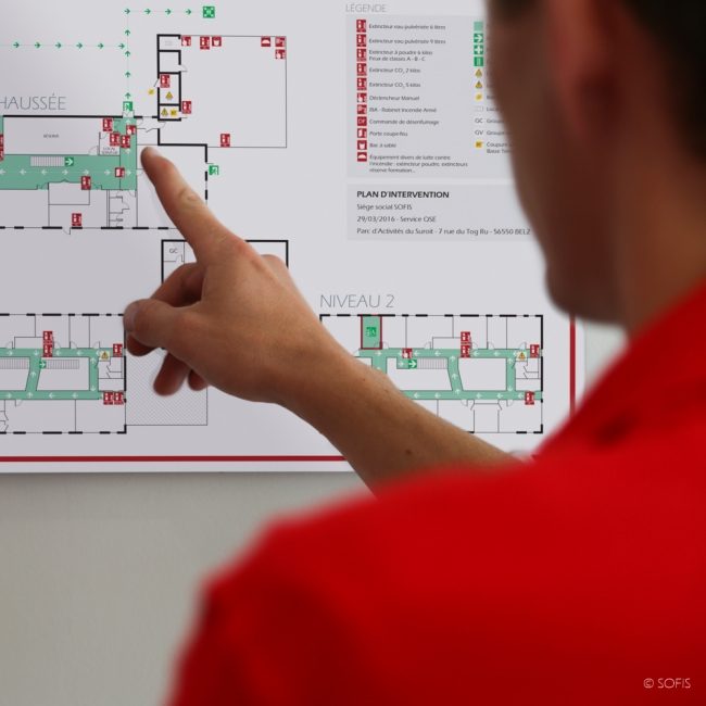 Person montrant un plan avec des indications et des zones colorées.