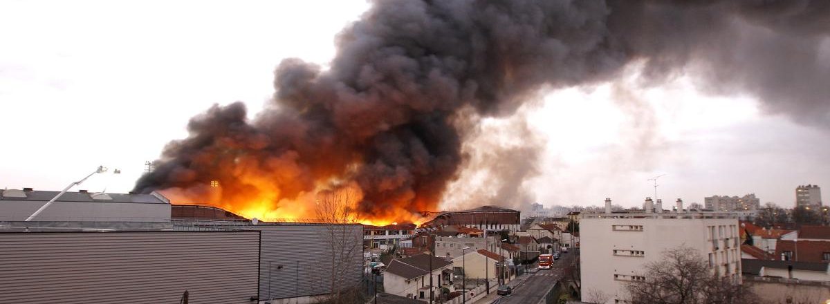 Un incendie intense dégage une épaisse fumée noire et des flammes illuminent le ciel.