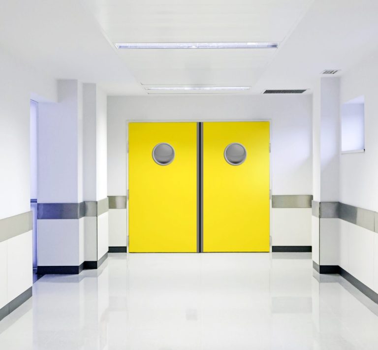 Deux grandes portes jaunes avec des hublots, dans un couloir lumineux et épuré.