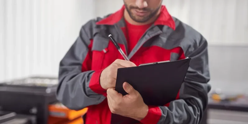 Un homme en uniforme rouge et gris prend des notes sur un carnet dans un environnement de travail.