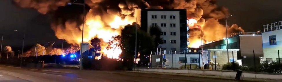 Incendie important près de bâtiments, avec des flammes et de la fumée visible.