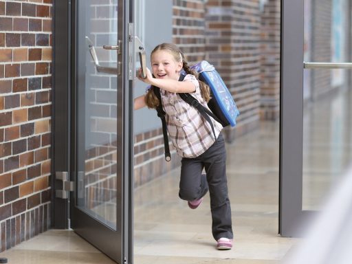 Petite fille souriante courant en ouvrant une porte, sac à dos sur le dos.