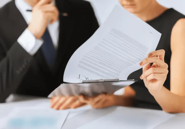 Deux personnes, en costume, examinent des documents ensemble.