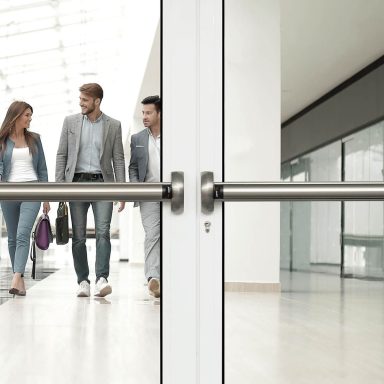 Trois personnes en costume marchant à travers une porte en verre dans un hall moderne.