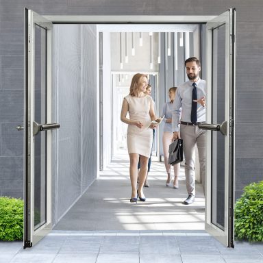 Deux personnes marchent à l'intérieur d'un hall d'entrée lumineux avec des portes ouvertes.
