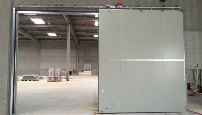 Grande porte coulissante grise dans un espace industriel vide.
