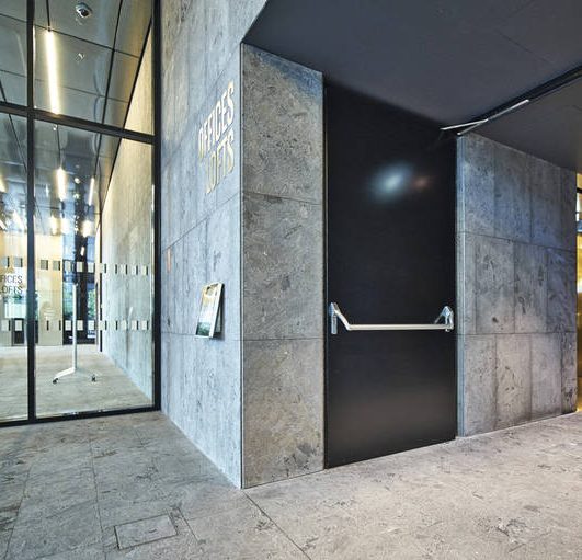 Porte noire dans un hall moderne avec des murs en marbre et des fenêtres en verre.