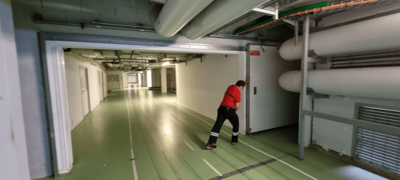 Un ouvrier en uniforme rouge pousse une porte dans un couloir de parking souterrain