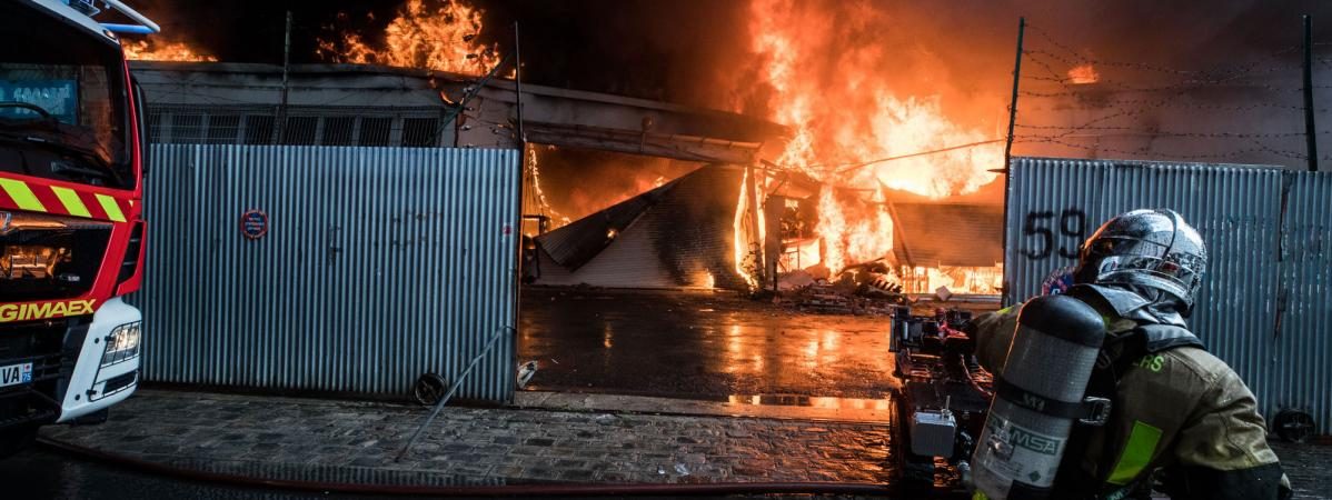 Pompiers combattent un incendie dans un bâtiment en feu, avec des flammes et de la fumée.
