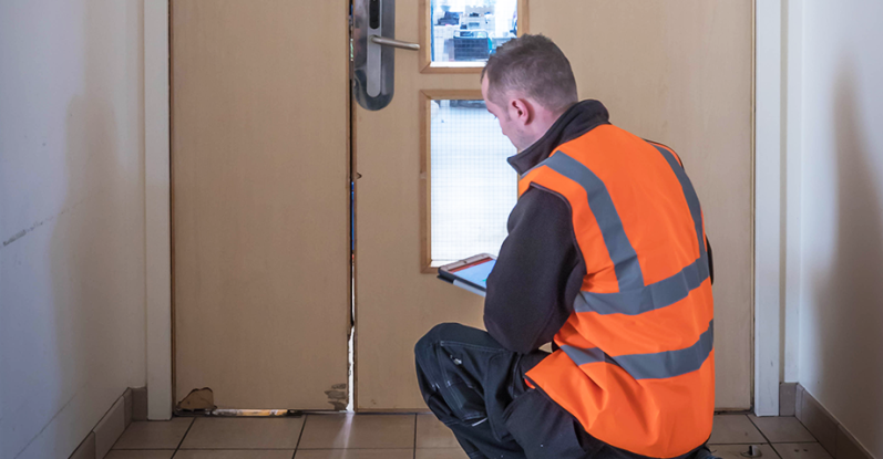 Un homme en gilet de sécurité assis près d'une porte, utilisant une tablette.