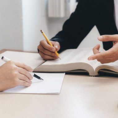Deux personnes discutent, une écrivant sur une feuille, l'autre tenant un livre ouvert.